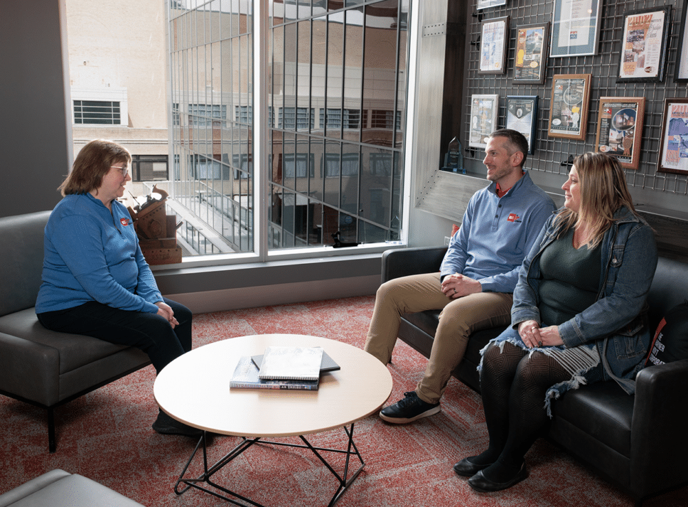 Three members of Hayner Hoyt's accounting and finance team sit around a coffee table having a conversation in a brightly lit room.