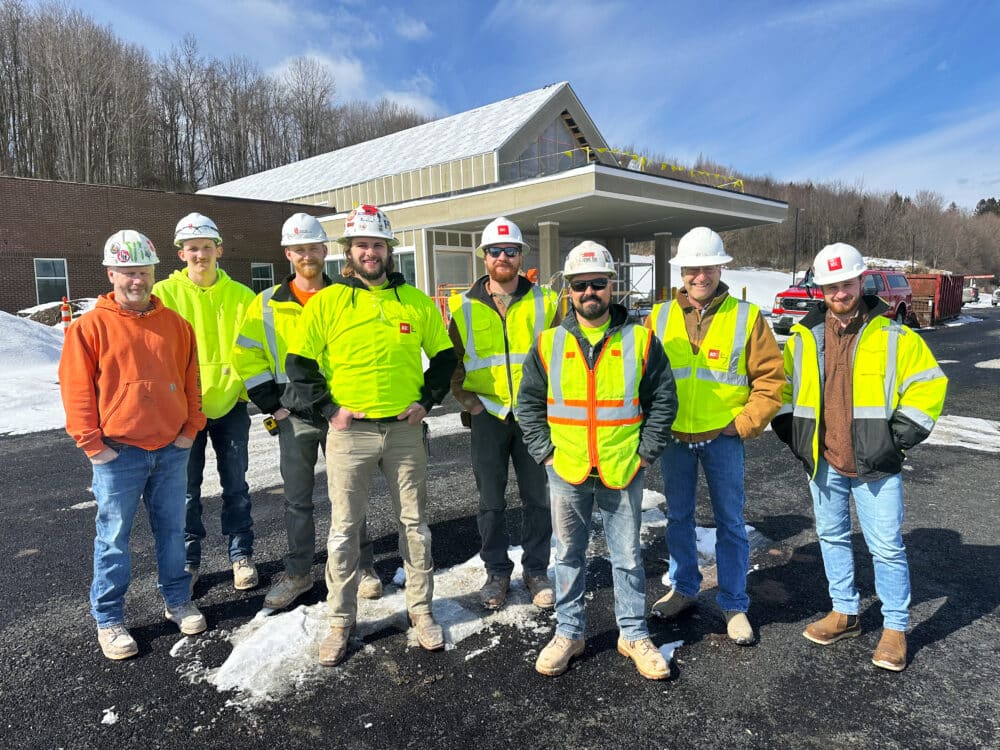 A group of Hayner Hoyt team members wearing high visibility yellow jackets, standing proudly in front of a new construction site.